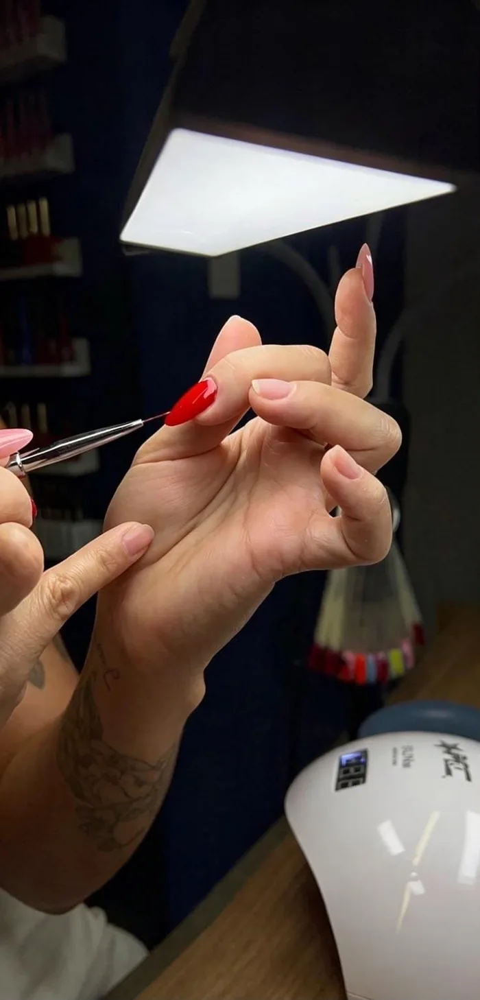 Maianne aplicando esmalte vermelho sob luz de cabine UV durante o atendimento